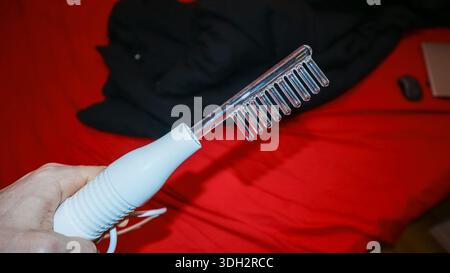 Schräge Ansicht der Finger, die tragbare Glasrechen auf roter Bettdecke mit dunklem Tuch in der Nähe greifen. Stockfoto