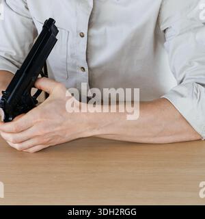 Kurzer Schuss des Unterarms in Hemdhülle auf Holztisch, während die schwarze halbautomatische Pistole seitlich gehalten wird. Stockfoto