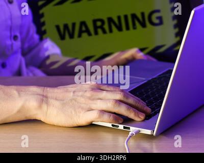 Nahaufnahme einer Person, die auf dem Laptop tippt, mit auffälligem grünem Warnschild im Hintergrund Stockfoto