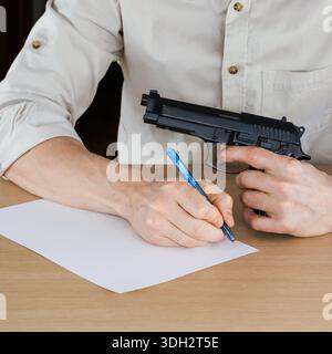 Nahaufnahme der Hände, die eine schwarze halbautomatische Pistole greifen, die auf einer hellen Holzoberfläche im Innenbereich aufliegt. Stockfoto