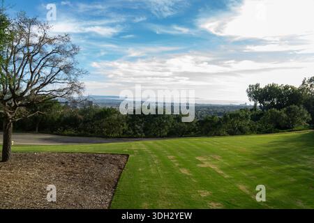 Eine weite Aussicht vom Getty Center in Los Angeles, Kalifornien, mit Blick auf grüne Rasenflächen, Bäume und die ferne Stadtlandschaft unter hellem Himmel. Stockfoto