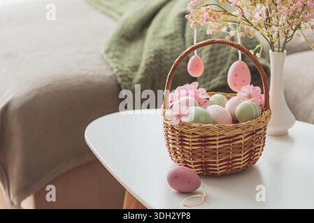 Osterkorb mit Ester-Eiern, Plüschhase und Frühlingsdekor auf weißem Tisch im Cozy Wohnzimmer Stockfoto