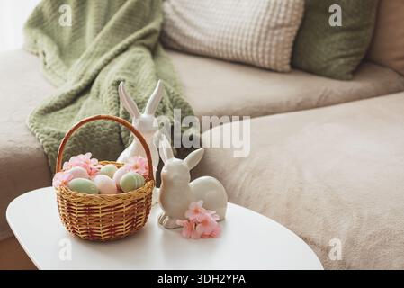 Osterkorb mit Ester-Eiern, Plüschhase und Frühlingsdekor auf weißem Tisch im Cozy Wohnzimmer Stockfoto