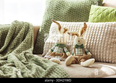 Gemütliches Sofa mit weichen Osterhasen-Puppen und strukturierten Kissen im Sonnenlicht Stockfoto