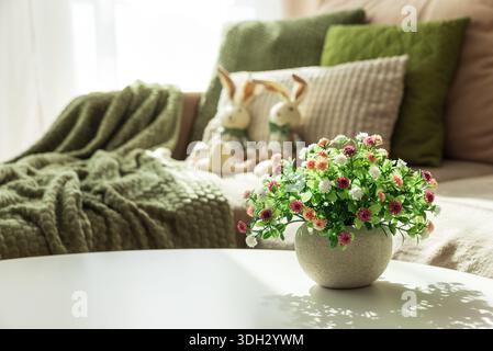 Gemütliches Oster-Wohnzimmer mit Plüschpuppen des Osterhasen und Frühlingsblumen auf dem Tisch Stockfoto