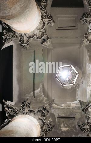 Blick nach oben auf die beleuchtete antike Laterne, umgeben von detaillierten Stuckarbeiten und korinthischen Säulenkapitellen im vernachlässigten historischen Eingang Stockfoto