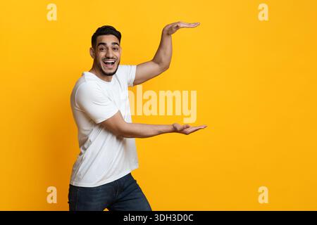 Staunende Mann aus dem Nahen Osten hält etwas Unsichtbares auf Gelb Stockfoto