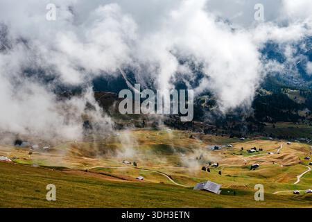 Dramatische Wolken ziehen über die sanften grünen Hügel und verstreuten traditionellen Almhütten von Seceda in den italienischen Dolomiten Stockfoto
