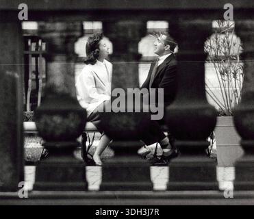 Das Foto zeigt einen Blick durch eine Steinschiene auf einen Mann und eine Frau, die auf einer Bank sitzen und sich zugewandt sind. Rizzuto, Angelo, 1906-1967, Fotograf. 1956. Stockfoto