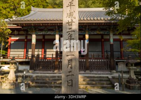 Kyoto, Japan - 16. Oktober 2023: Eine hohe Holzsäule mit japanischen Schriftzeichen steht im Vordergrund vor der Haupthalle von Zenrinjiamidado im Zenrin-JI-Tempel, mit Steinlaternen, Stufen und traditioneller Architektur. Stockfoto
