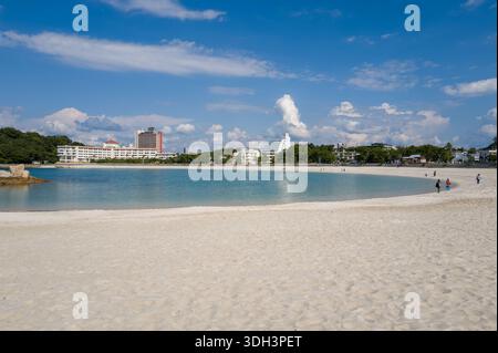Shirarahama, Japan - 25. Oktober 2023: Ein weiträumiger weißer Sandstrand mit türkisfarbenem Wasser, ein paar Menschen entlang der Küste und mehrere moderne Gebäude und Hotels, die im Hintergrund unter blauem Himmel mit verstreuten Wolken zu sehen sind. Stockfoto