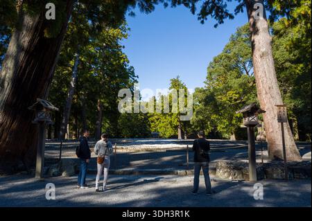 ISE, Japan - 29. Oktober 2023: Drei Personen stehen am Eingang des ehemaligen Kodenchi-Schreins, umgeben von hohen Bäumen und Kies, mit Holzlaternen und einem Schild sichtbar. Stockfoto