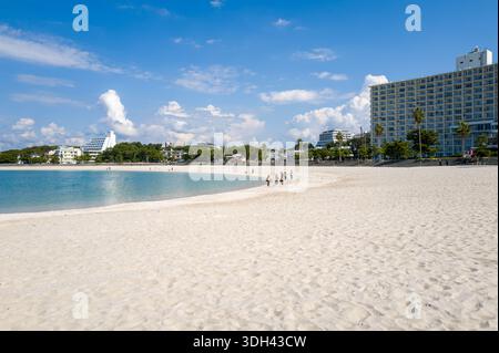 Shirarahama, Japan - 25. Oktober 2023: Ein breiter weißer Sandstrand mit ein paar Leuten, die in der Nähe der Küste spazieren, türkisfarbenes Wasser und mehrere moderne Gebäude und Hotels im Hintergrund unter einem blauen Himmel mit verstreuten Wolken. Stockfoto