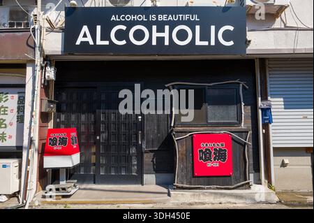 Shirarahama, Japan - 25. Oktober 2023: An der Außenseite einer Bar befindet sich ein großes Schild mit der Aufschrift „ALCOHOL IS BEAUTIFUL ALCOHOL“ über dem Eingang, mit zusätzlichen japanischen Schildern und einer geschlossenen schwarzen Tür bei Tageslicht. Stockfoto