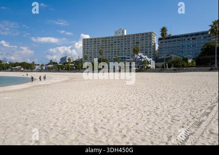 Shirarahama, Japan - 25. Oktober 2023: Ein breiter weißer Sandstrand mit ein paar Leuten, die in der Nähe der Küste spazieren, türkisfarbenes Wasser und mehrere moderne Gebäude und Hotels im Hintergrund unter einem blauen Himmel mit verstreuten Wolken. Stockfoto
