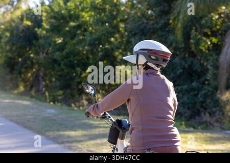 Eine Nahaufnahme eines Radfahrers, der auf einem befestigten Naturlehrpfad fährt. Der Fahrer trägt einen weißen Schutzhelm über einer Sonnenblende und einem lila Long-slee Stockfoto