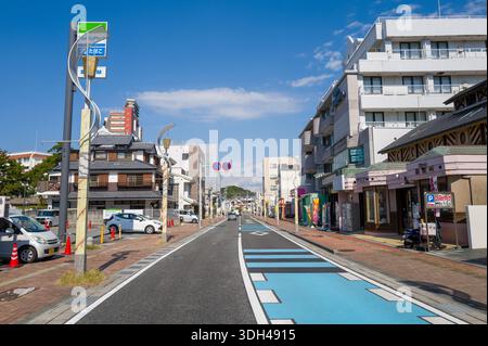 Shirarahama, Japan - 25. Oktober 2023: Eine breite Straße, gesäumt von Geschäftsgebäuden, Geschäften, geparkten Autos und sichtbaren Schildern, einschließlich eines FamilyMart-Schildes, unter einem klaren blauen Himmel im Stadtzentrum. Stockfoto