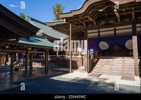 ISE, Japan - 29. Oktober 2023: Der Innenhof und die Eingangstreppe der Kaguraden Hall in Ise Jingu werden mit traditioneller Holzarchitektur, lila Vorhänge mit weißen Emblemen und goldenen dekorativen Elementen unter einem klaren blauen Himmel gezeigt. Stockfoto