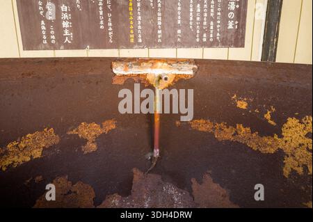 Shirarahama, Japan - 25. Oktober 2023: Nahaufnahme eines alten, verrosteten Metallbehälters mit Rohrbefestigung, der sich unter einem japanischen Informationsschild an einer Wand befindet. Stockfoto