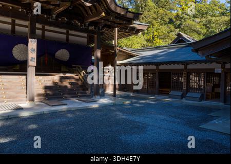 ISE, Japan - 29. Oktober 2023: Das Äußere der Kaguraden Halle ist mit Holzarchitektur, lila Vorhängen mit Chrysanthemen-Wappen und umliegenden Gebäuden mit Bäumen im Hintergrund zu sehen. Stockfoto