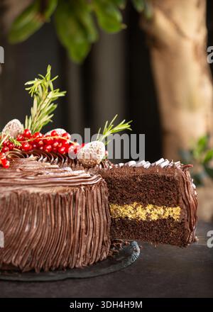 Eine Nahaufnahme eines festlichen Schokoladenkuchens in Scheiben geschnitten, dekoriert mit roten Johannisbeeren, Rosmarin und gezuckerten Tannenzapfen. Stockfoto