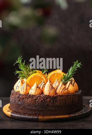 Ein reichhaltiger Schokoladenkuchen mit orangefarbenen Meringue-Strudeln, die mit Schokolade getränkt sind, verziert mit frischen Orangenscheiben und Rosmarinzweigen. Stockfoto