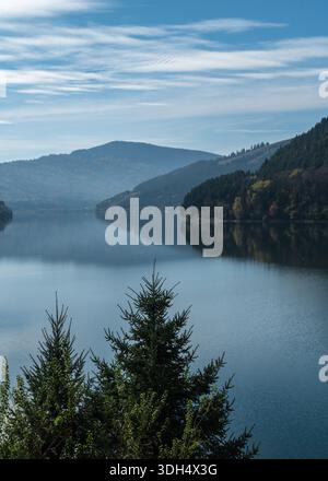 Ein ruhiger Blick auf den See Izvorul Muntelui, der an einem sonnigen Herbsttag in der Region Neamt in Rumänien die mit Kiefern bedeckten Karpaten reflektiert Stockfoto