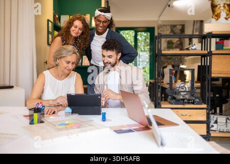 Ein vielfältiges Team von Kollegen arbeitet in einem modernen Coworking-Bereich zusammen. Sie versammeln sich an einem Tisch mit Laptops und einem Tablet, tauschen Ideen und Fosterin aus Stockfoto