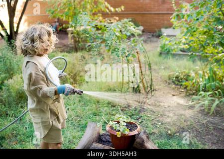 Eine ältere Frau pflegt ihren städtischen Garten und tränkt an einem sonnigen Tag Topfpflanzen. Ihre pflegende Berührung und ihre erfahrenen Hände bringen Vitalität und Leben Stockfoto