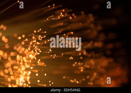 Eine Nahaufnahme von Glasfasersträngen, die vor dunklem Hintergrund warm-Golden leuchten. Das Licht erzeugt einen abstrakten Effekt, der ein Gefühl von Tiefe und Mys verleiht Stockfoto