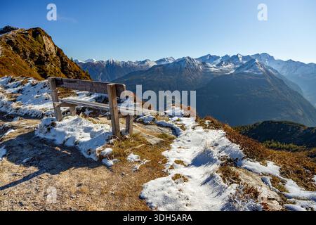 Ein malerischer Blick auf die europäischen Alpen im Herbst mit schneebedeckten Gipfeln und einer rustikalen Holzbank mit Blick auf die ruhige Berglandschaft Stockfoto