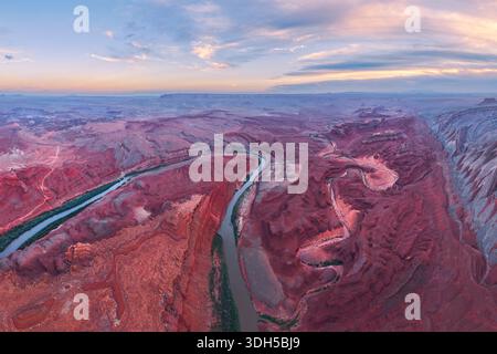 Blick aus der Vogelperspektive auf den San Juan River, der sich bei Sonnenuntergang durch die atemberaubende rote Felsenlandschaft von Utah, USA, schlängelt. Das Bild zeigt die dramatische Landschaft und Stockfoto