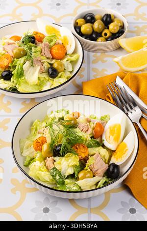 Ein farbenfroher Salat mit Eisberg- und Römersalat, hart gekochten Eiern, Thunfisch aus der Dose, schwarzen und grünen Oliven und einem Hauch Dill-Beilage, perfekt für Stockfoto