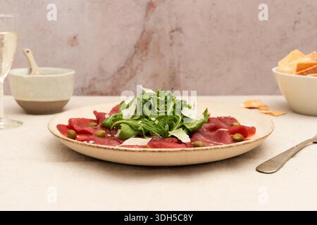 Ein zarter Teller mit Rindfleisch-Carpaccio, belegt mit frischem Rucola und geriebenem Käse. Das sorgfältig arrangierte Gericht ist eine perfekte Mischung aus Aromen und Eleganz Stockfoto