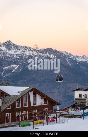 Eine faszinierende Winterszene in den italienischen Alpen bietet schneebedeckte Gipfel, ein bezauberndes Holzchalet und eine Seilbahn, die unter dem pastellfarbenen Schein ragt Stockfoto