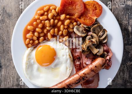 Komplettes englisches Frühstück mit Spiegelei, Speck, Würstchen und Bohnen auf Holztisch Stockfoto