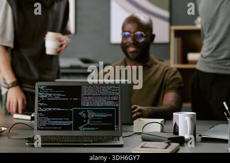 Junger Erwachsener Schwarzer Mann lächelt während der Zusammenarbeit im modernen Office Workspace Stockfoto