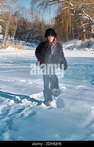 Das Bild fängt einen wunderbaren Wintermoment ein, in dem eine Frau in einem stilvollen Pelzmantel und Hut einen verschneiten Tag genießt und verspielt weht Stockfoto