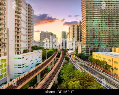 Eisenbahngleise und öffentliche Bahnlinien führen durch das Zentrum von Miami Brickell in Florida, USA, umgeben von Sonnenuntergang beleuchteten Wolkenkratzern der Stockfoto