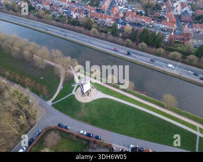 Blick aus der Vogelperspektive auf eine historische Windmühle, die stolz an einem Kanal steht, im Kontrast zu der modernen Straße mit viel Verkehr, Brügge, Flandern, Belgien. Stockfoto