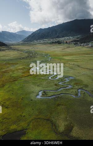 Aus der Vogelperspektive auf einen Serpentinfluss, der sich durch den üppig grünen Talboden schlängelt, umgeben von den majestätischen Bergen, Phobjikha Valley, Wangdue Phodrang, Stockfoto