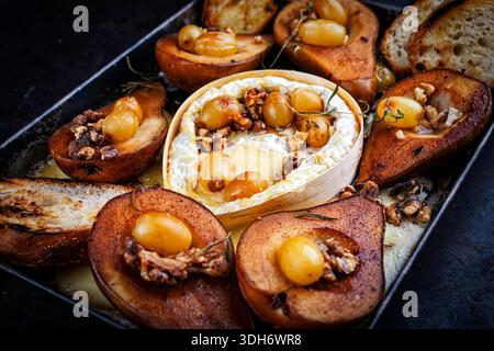 Im Ofen gebackener Camembert-Käse mit karamelisierten glasierten Birnen, Walnüssen und Trauben sowie Baguette auf rustikalem Metallteller Stockfoto