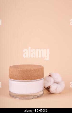 Ein Glas mit Feuchtigkeitscreme und Baumwollzweig auf beigefarbenem Hintergrund. Naturschönheitsprodukt, Bio-Kosmetik kreatives Konzept. Detaillierter Behälter aus weißem Glas Stockfoto