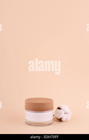 Ein Glas mit Feuchtigkeitscreme und Baumwollzweig auf beigefarbenem Hintergrund. Naturschönheitsprodukt, Bio-Kosmetik kreatives Konzept. Detaillierter Behälter aus weißem Glas Stockfoto