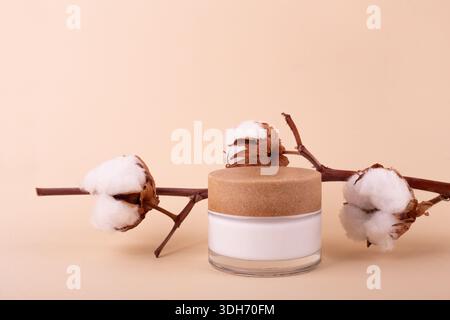 Ein Glas mit Feuchtigkeitscreme und Baumwollzweig auf beigefarbenem Hintergrund. Naturschönheitsprodukt, Bio-Kosmetik kreatives Konzept. Detaillierter Behälter aus weißem Glas Stockfoto
