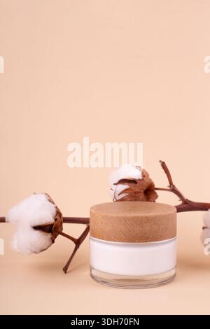 Ein Glas mit Feuchtigkeitscreme und Baumwollzweig auf beigefarbenem Hintergrund. Naturschönheitsprodukt, Bio-Kosmetik kreatives Konzept. Detaillierter Behälter aus weißem Glas Stockfoto