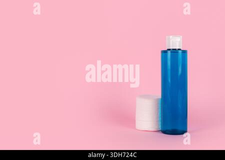 Make-up-Entferner in blauer Plastikflasche auf rosafarbenem Hintergrund, kosmetische Wattepads. Natürliches organisches Schönheitsprodukt. Mizellarwasser zur Reinigung Stockfoto