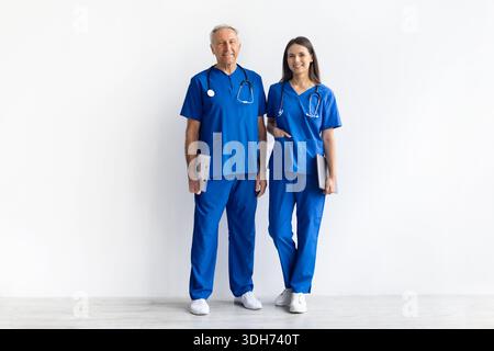 Leitender männlicher Arzt und junge weibliche Ärztin, die in blauen medizinischen Peelings steht Stockfoto