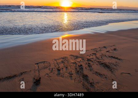 Das Wort 'FRIEDEN' schrieb in den Sand an einem ruhigen Strand mit Sonnenuntergang über den Meereswellen, was eine Botschaft der Harmonie schafft. Stockfoto