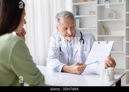 Oberarzt, der dem Patienten während der Sprechstunde die medizinische Form erklärt Stockfoto